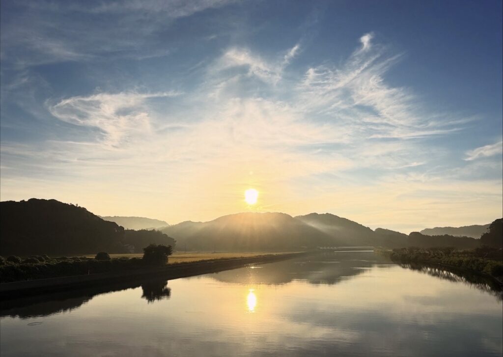 逆光で山々を“縁どり”、朝陽を水面に映す。空の面積を多めに取り、雲形を主役に構成